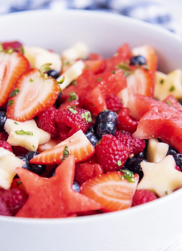 A bowl of a fruit salad for fourth of july with strawberries, blueberries, apples, watermelon, and raspberries, in a mint honey lime sauce.