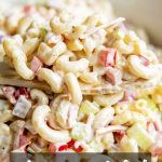 A large spoonful of macaroni salad just out of the bowl of the creamy salad, with a text overlay for pinterest saying "macaroni salad"