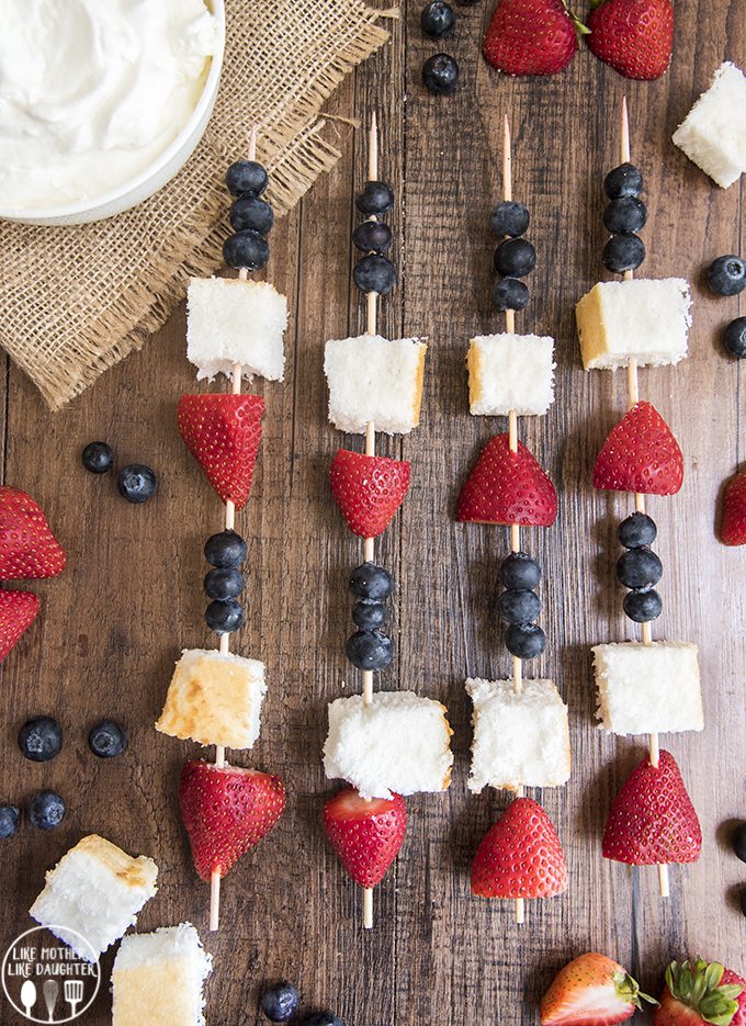 Red, white, and blue fruit kebabs above image on a wood background.