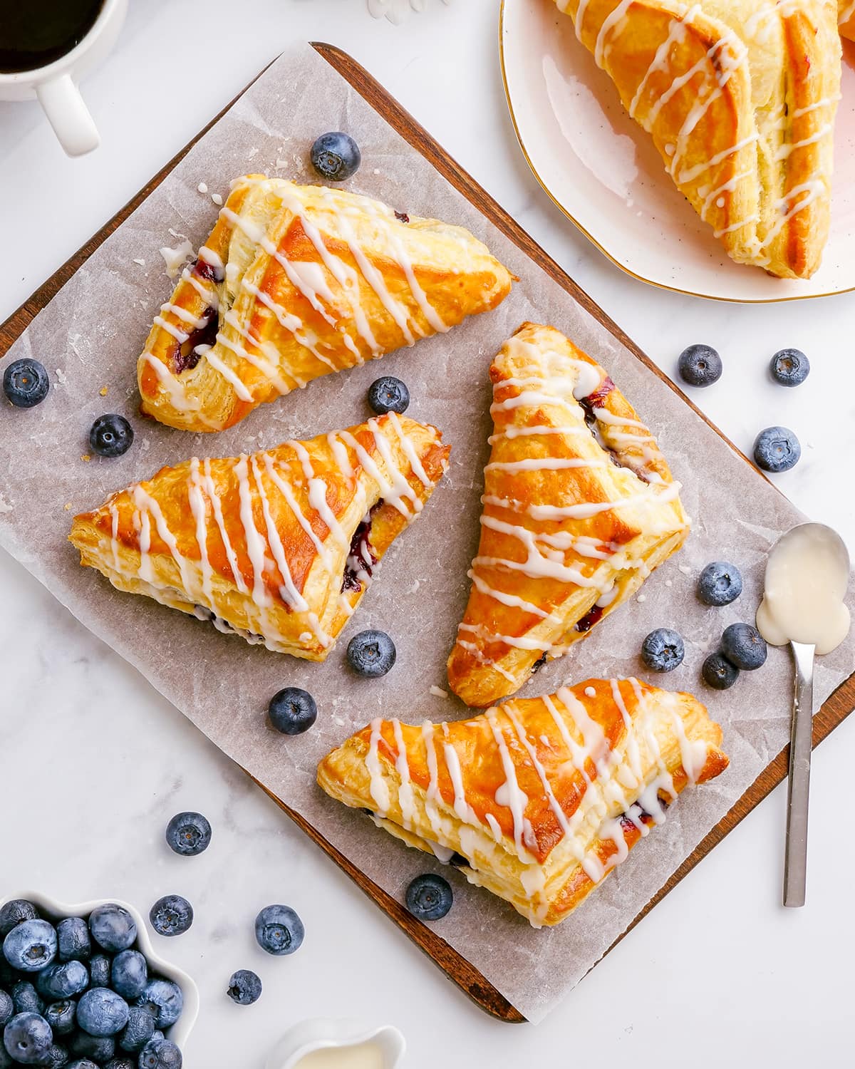 Four blueberry turnovers on a wooden tray, each drizzled with a powdered sugar glaze over the top.