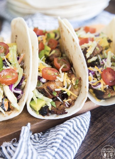 Close up of three bbq pork tacos filled with meat and cheese and tomatoes.