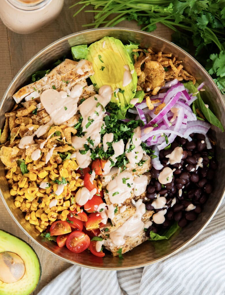 A BBQ Ranch Chicken Salad with the ingredients separated on top of the salad, corn, tomatoes, chicken, avocado, red onion, black beans, corn, and fried onions.