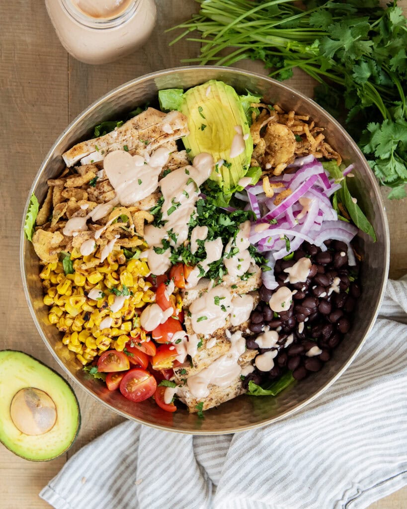 A BBQ Ranch Chicken Salad with the ingredients separated on top of the salad, corn, tomatoes, chicken, avocado, red onion, black beans, corn, and fried onions.