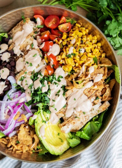 A BBQ Ranch Chicken Salad with the ingredients separated on top of the salad, corn, tomatoes, chicken, avocado, red onion, black beans, corn, and fried onions.