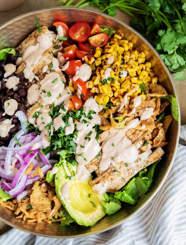 A BBQ Ranch Chicken Salad with the ingredients separated on top of the salad, corn, tomatoes, chicken, avocado, red onion, black beans, corn, and fried onions.