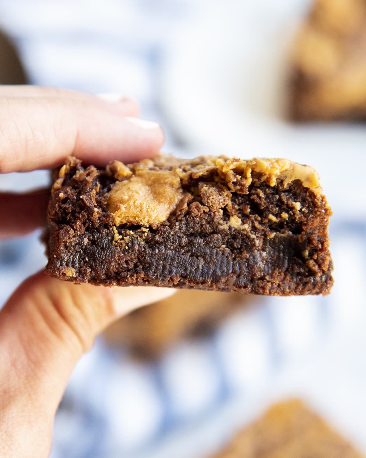 A hand holding a fudgy brownie topped with butterfinger swirls.
