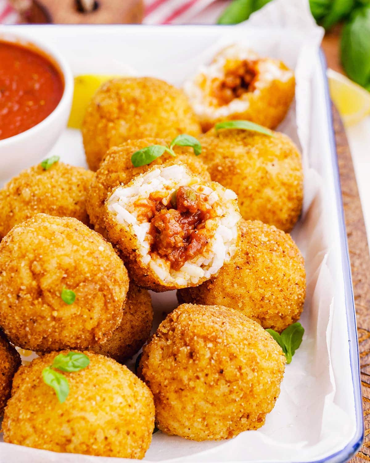 A pile of arancini rice balls, and one is bit into showing the ragu filling.