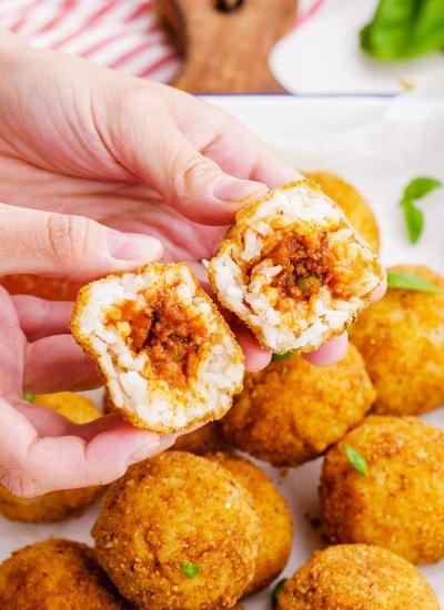 A hand holding two halves of an arancini rice ball showing the meat sauce in the middle.
