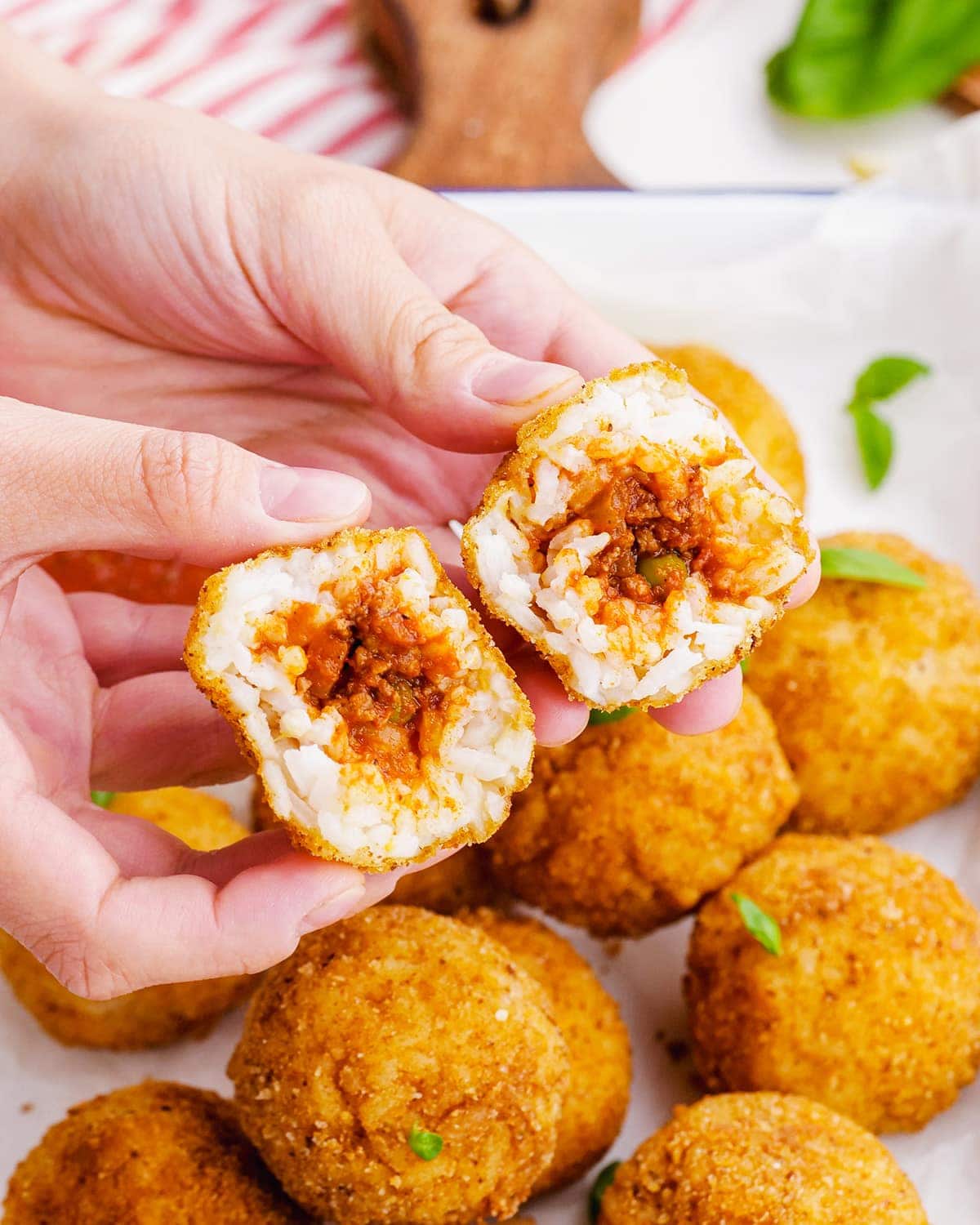 A hand holding two halves of an arancini rice ball showing the meat sauce in the middle.