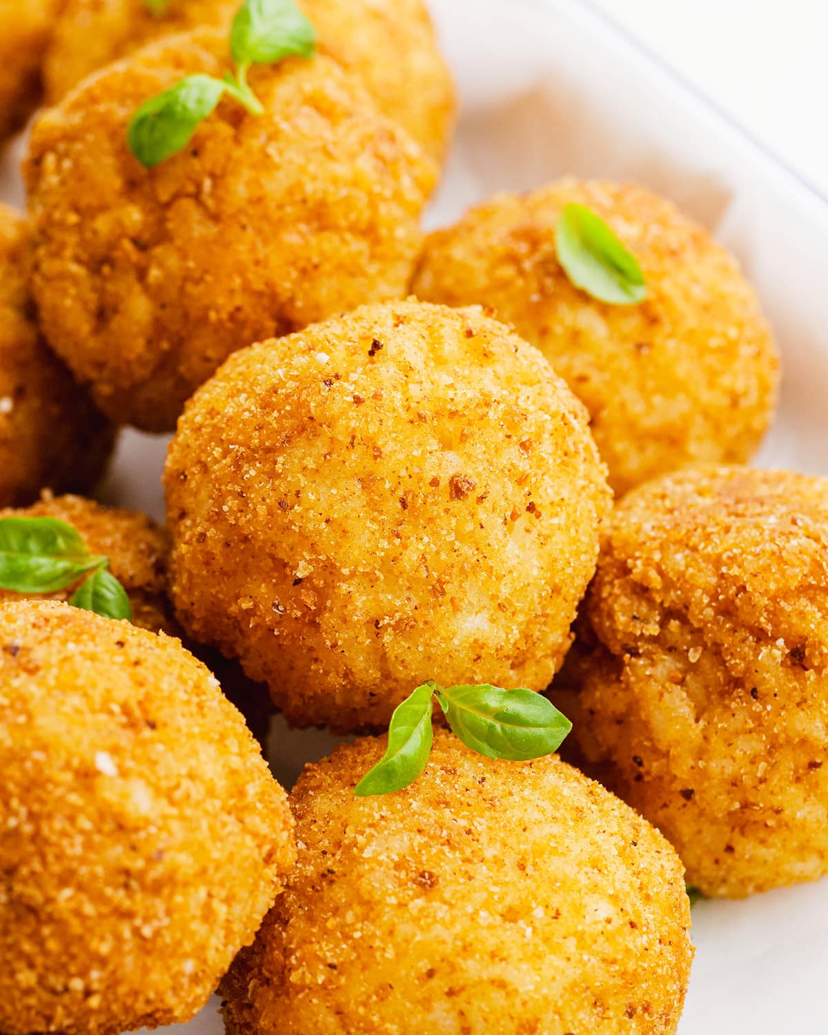 A close up of arancini balls in a pile, with small basil leaves among them.