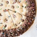 An above shot of giant chocolate chip cookie cake with sprinkles on top and chocolate frosting.