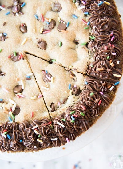 An above shot of giant chocolate chip cookie cake with sprinkles on top and chocolate frosting.