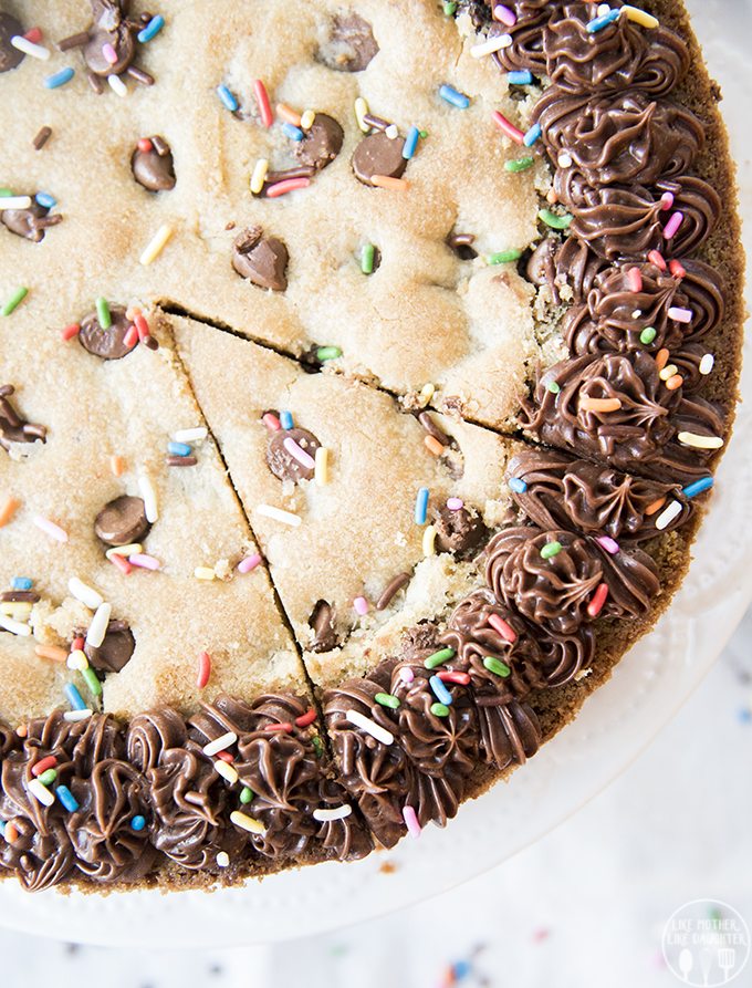 An above shot of giant chocolate chip cookie cake with sprinkles on top and chocolate frosting.