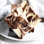 A cheesecake swirled brownie with cheesecake and brownie marbled together, set on a plate.