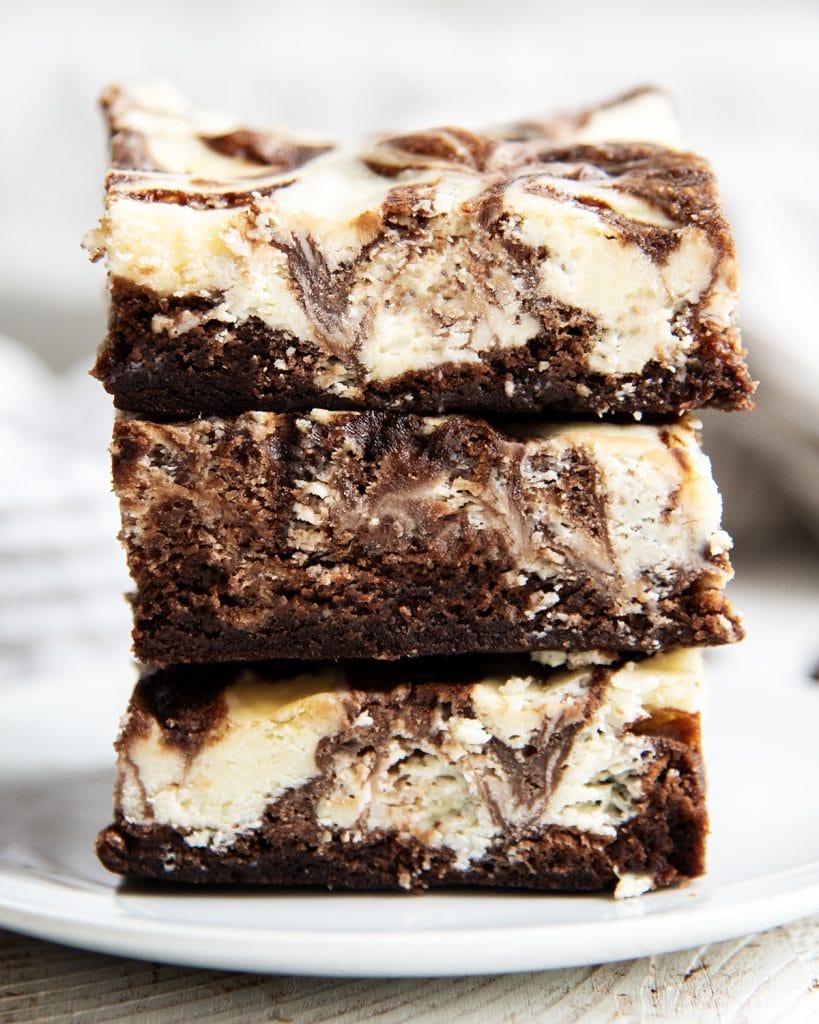 A stack of three cheesecake brownies on a white plate.