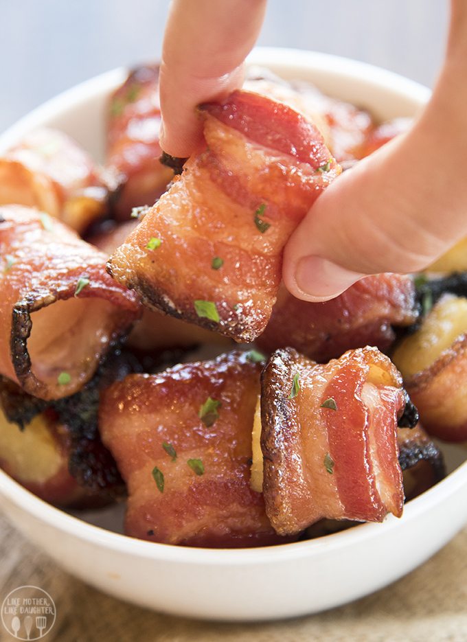 Pineapple pieces wrapped in bacon all in a bowl. Fingers are grabbing one of the bites.