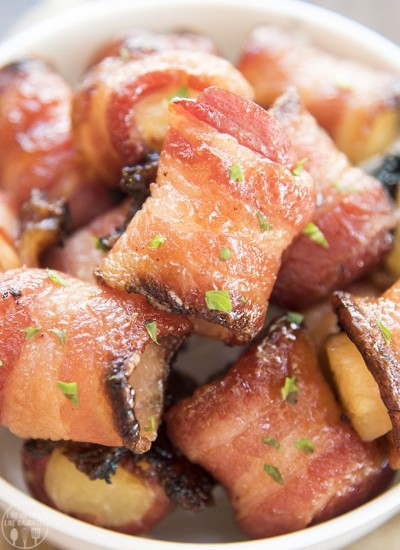 Bacon wrapped pineapple bites in a bowl topped with fresh herbs.