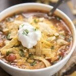 A bowl of enchilada soup topped with tortilla strips, cheese, and a scoop of sour cream.