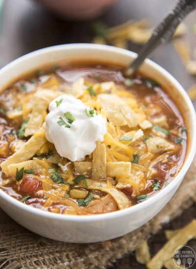 A bowl of enchilada soup topped with tortilla strips, cheese, and a scoop of sour cream.
