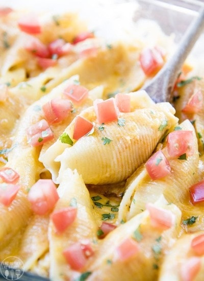 A spoonful cutting into a pan of chicken enchilada stuffed shells topped with diced tomatoes.