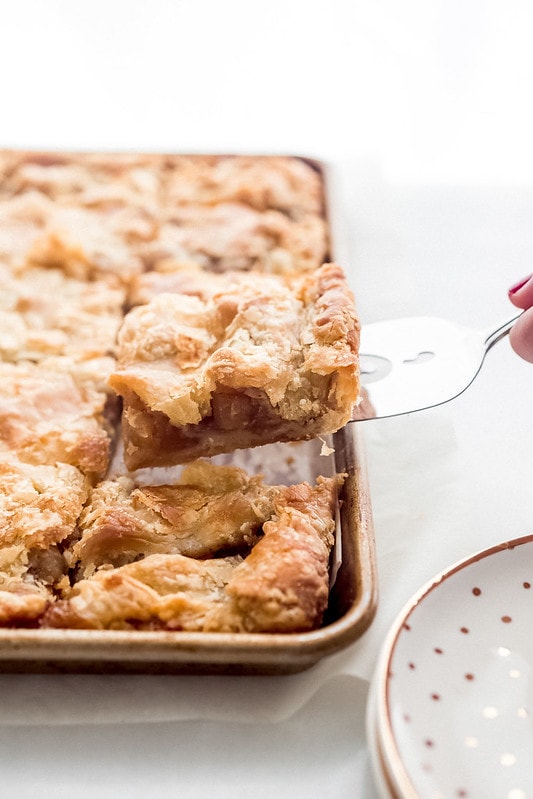 An apple slab pie in a cookie sheet with a piece being lifted up on a spatula.