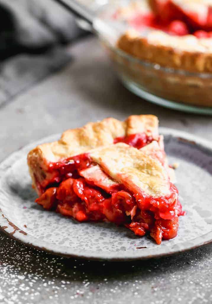 A big slice of cherry pie on a grey stoneware plate.