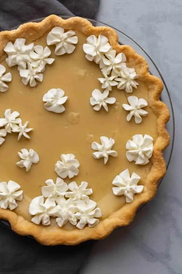 An overhead shot of a pie filled with custard and topped with whipped cream flowers.