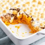 A close up of some sweet potato casserole, showing the layers of the mashed sweet potatoes, candied pecans, and toasted marshmallows.