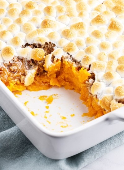 A close up of some sweet potato casserole, showing the layers of the mashed sweet potatoes, candied pecans, and toasted marshmallows.