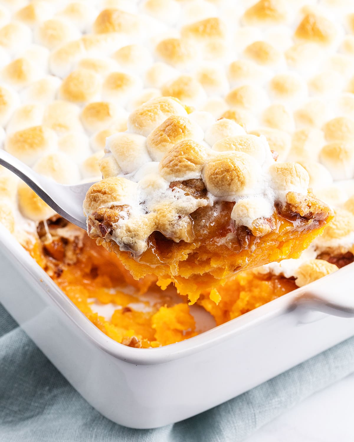 A large spoonful of sweet potato casserole being lifted out of the pan.
