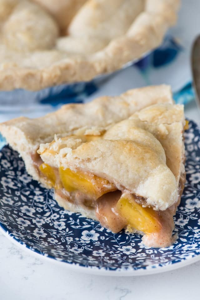 A slice of peach pie with a double crust on a blue and white floral plate.