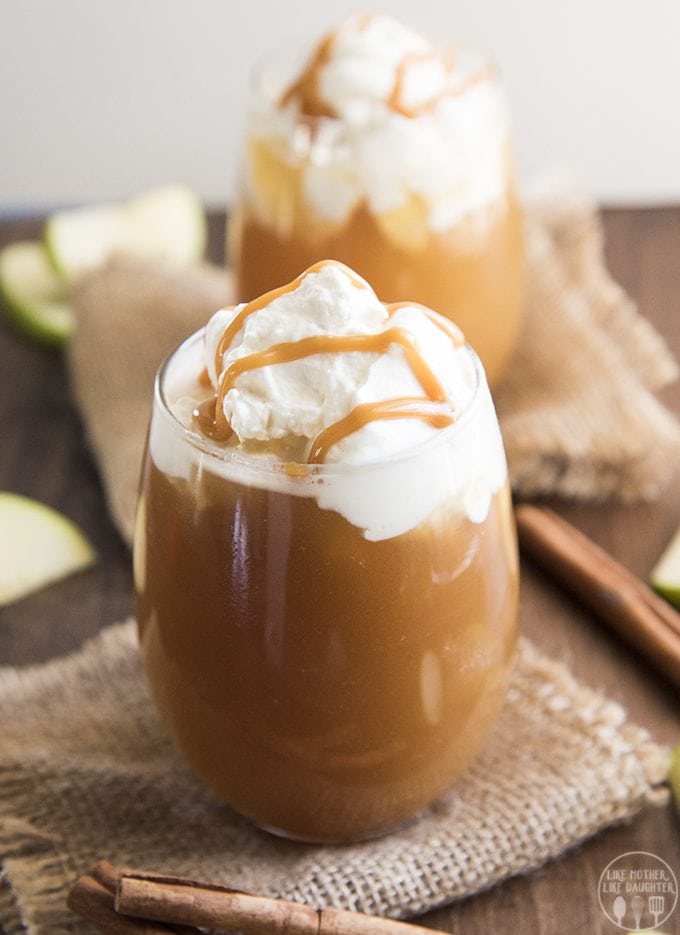 Two glasses of a caramel apple drink topped with whipped cream and melted caramel.