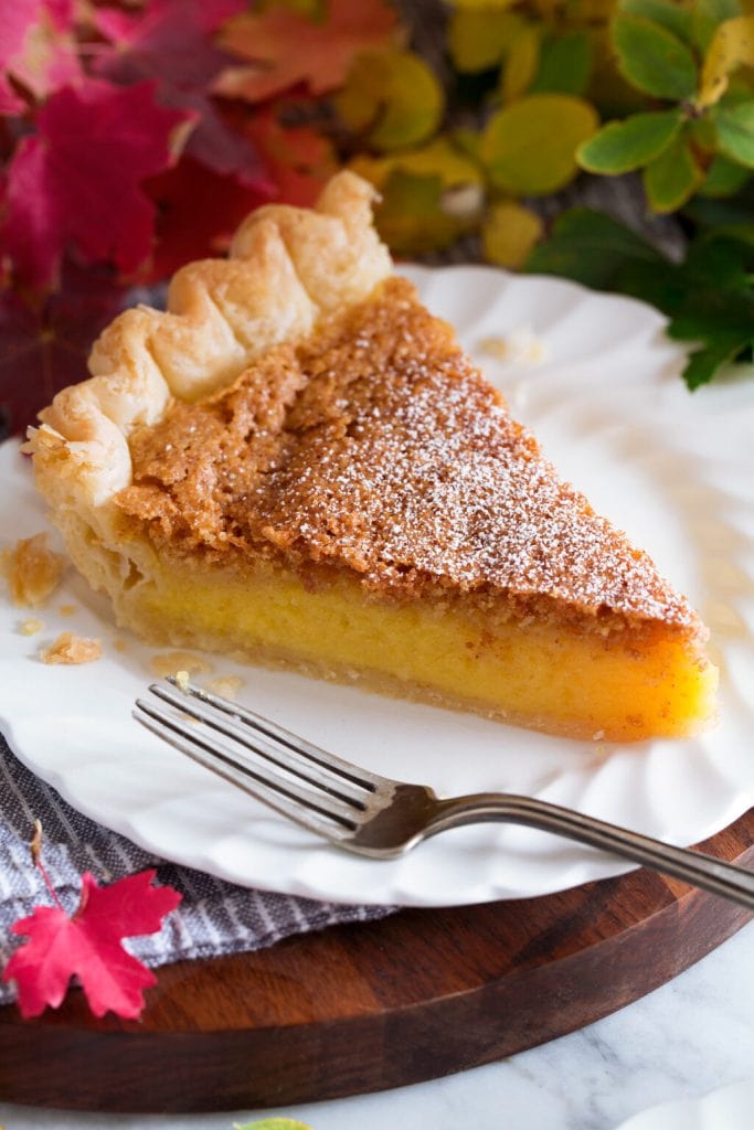 A slice of chess pie with a crunchy crust on the top, and a fork laying next to it on a plate. 