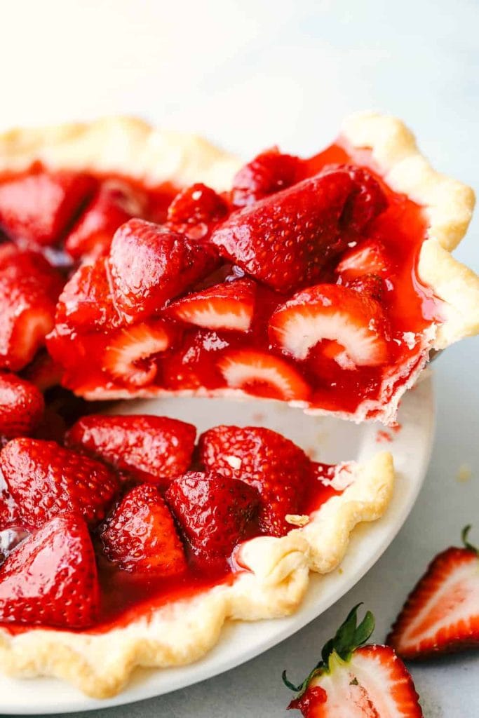 A fresh strawberry pie with a slice being lifted out of the pie.