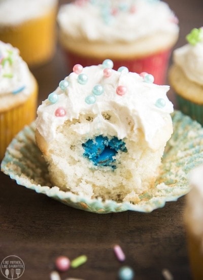 A cupcake with a bite out of the middle showing blue m&ms in the middle.