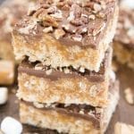 A stack of caramel rice krispie treats topped with chocolate and pecans.