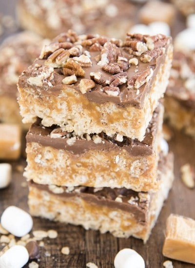 A stack of caramel rice krispie treats topped with chocolate and pecans.