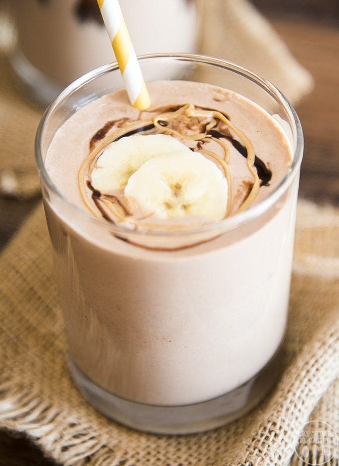 A glass of a chocolate smoothie topped with bananas and a peanut butter swirl.