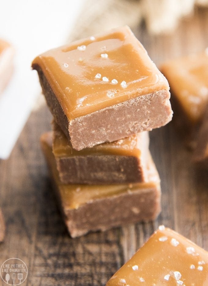 A stack of caramel topped fudge pieces with coarse sea salt on top. 