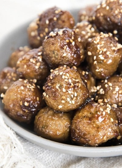 A close up of teriyaki meatballs in a bowl sprinkled with toasted sesame seeds.