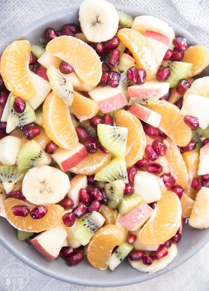 A bowl of fruit salad with pomegranate seeds, oranges, kiwi, banana, and apples.