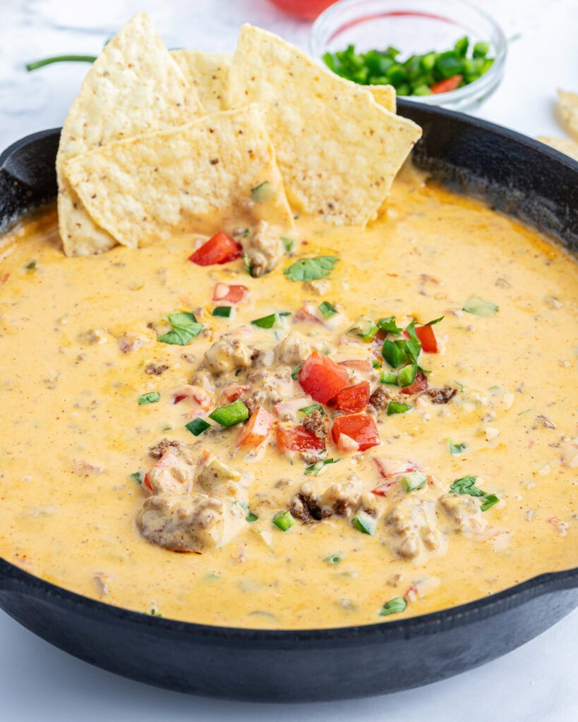 A skillet of queso dip topped with diced tomatoes, jalapenos, and with tortilla chips.