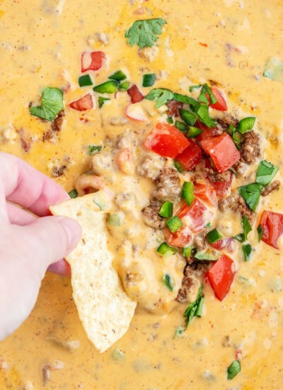 A hand dipping into a skillet of beef queso dip.