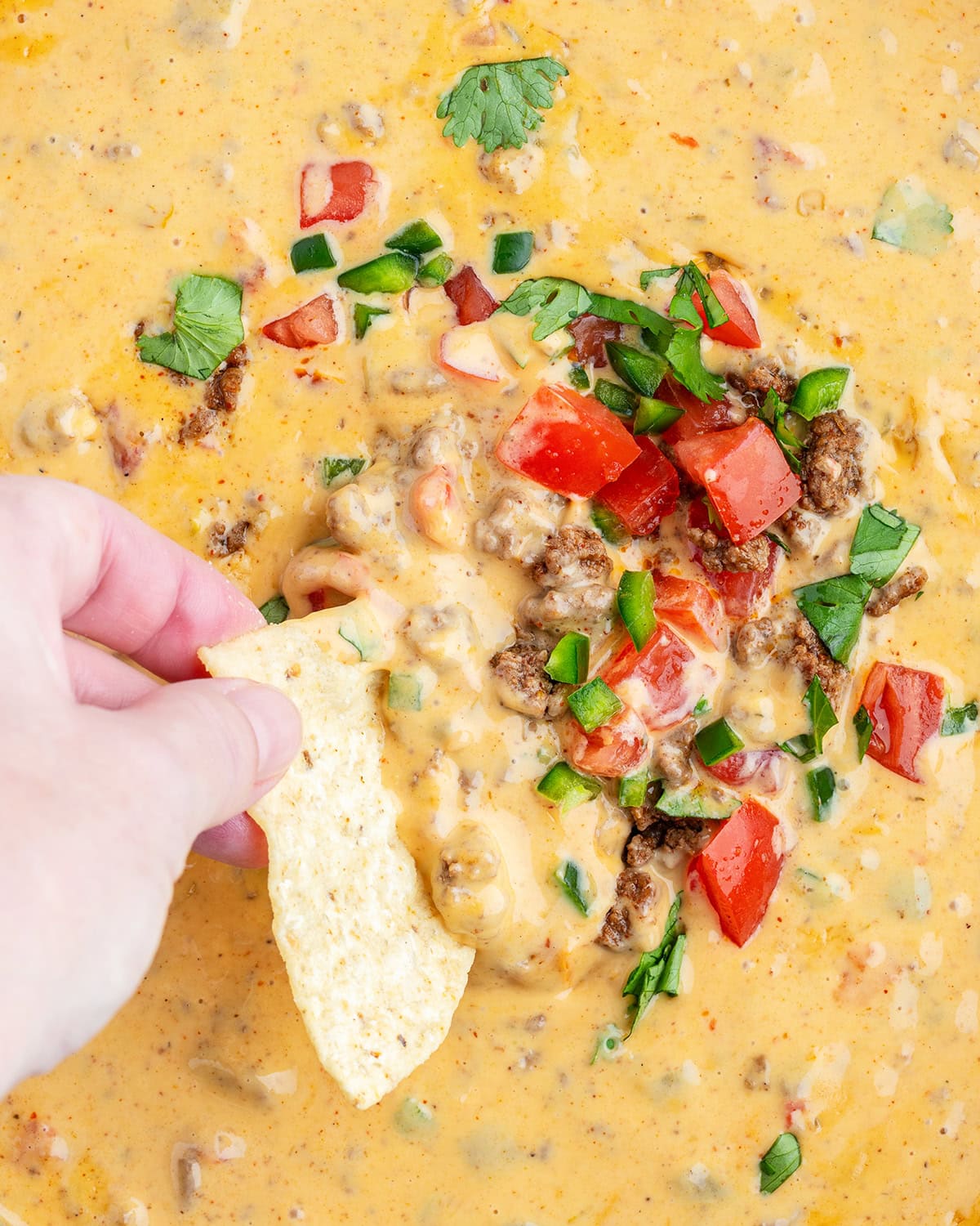 A hand dipping into a skillet of beef queso dip.