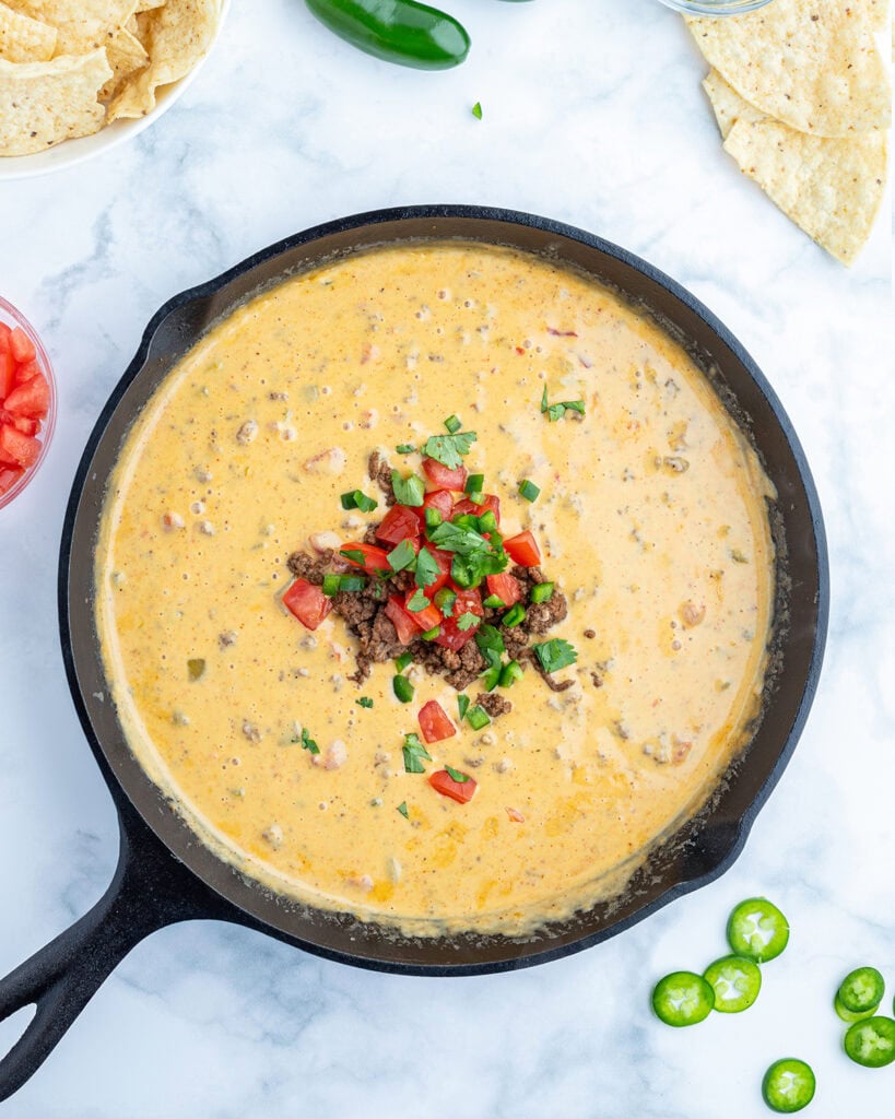 An above view of a skillet of beef queso dip topped with ground beef, diced tomatoes, and jalapenos.