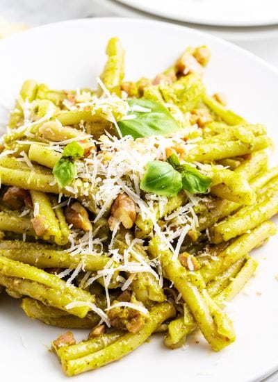 A plate of Casarecce Pasta with pesto sauce topped with shredded parmesan, and fresh basil.