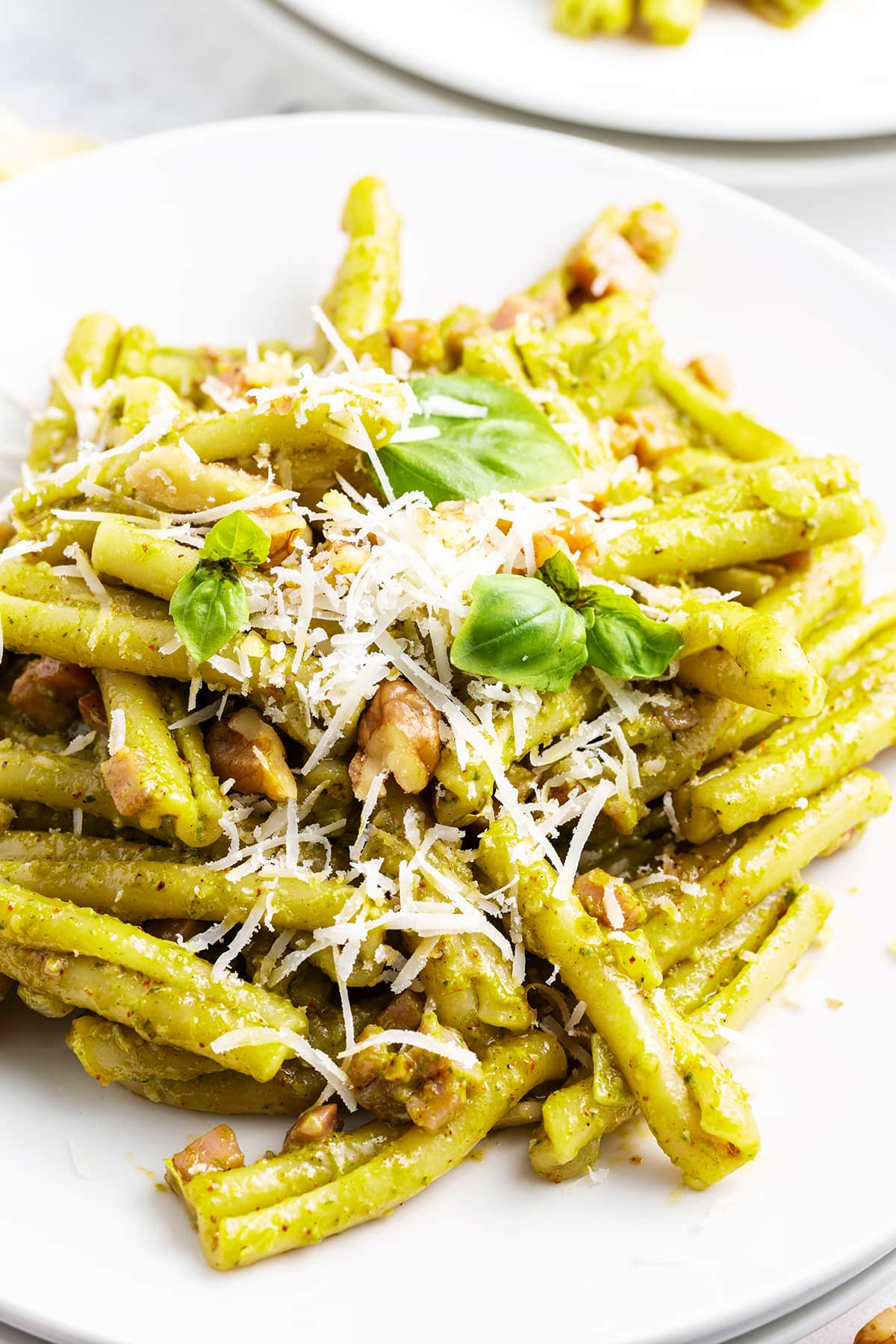A plate of Casarecce Pasta with pesto sauce topped with shredded parmesan, and fresh basil.