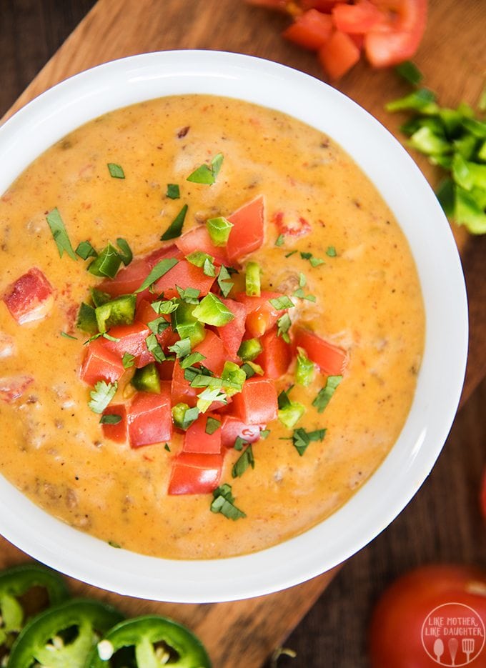 A close up of a bowl of cheese dip topped with tomatoes and diced jalapenos. 