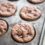 A muffin pan with chocolate banana muffins with chocolate chips in them.