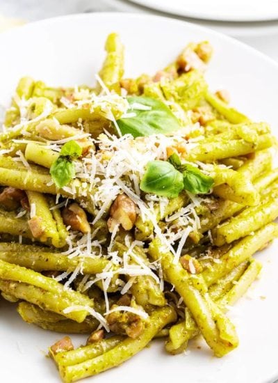 A plate of Casarecce Pasta with pesto sauce topped with shredded parmesan, and fresh basil.